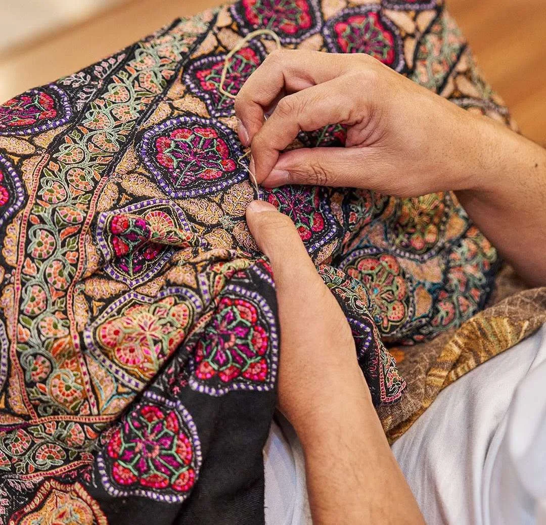 A Kashmiri artisan working delicate stitches into a richly patterned shawl